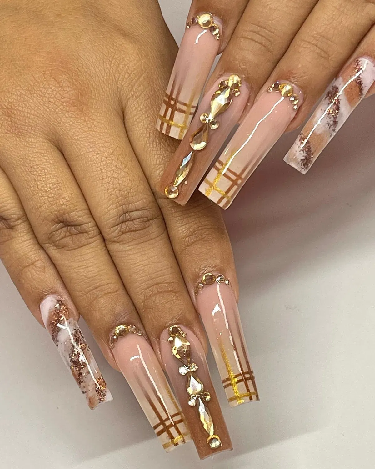 Pale nude coffin nails with tip plaid lines and prominent rhinestone embellishments