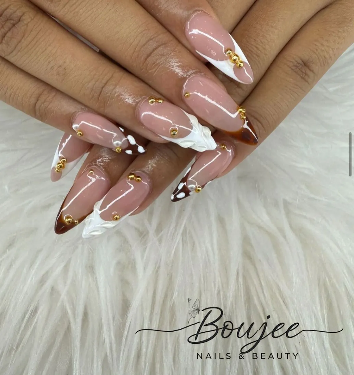 Nude stiletto nails with brown/white swirls, gold beads, and a 3D white accent