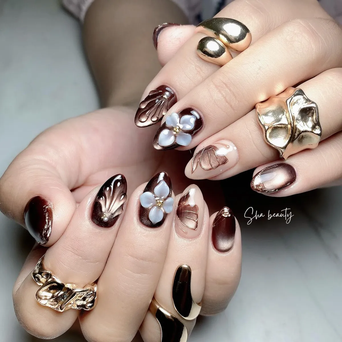 Deep brown and bronze nails with sculpted shell textures and 3D flowers