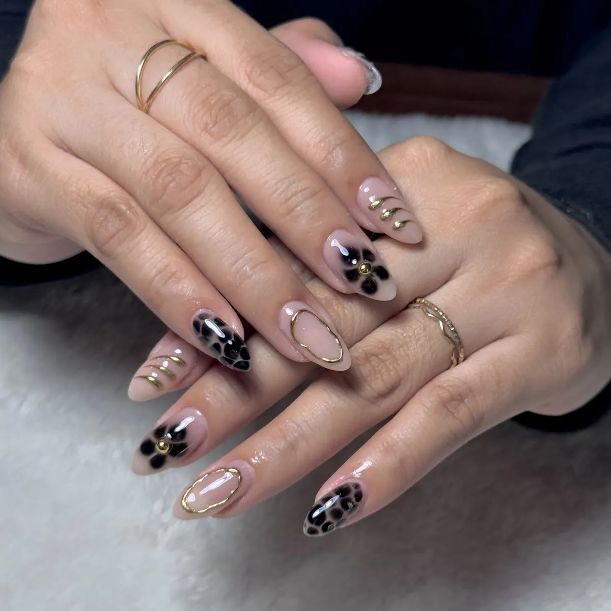 Nude almond nails with black florals and gold outline accents