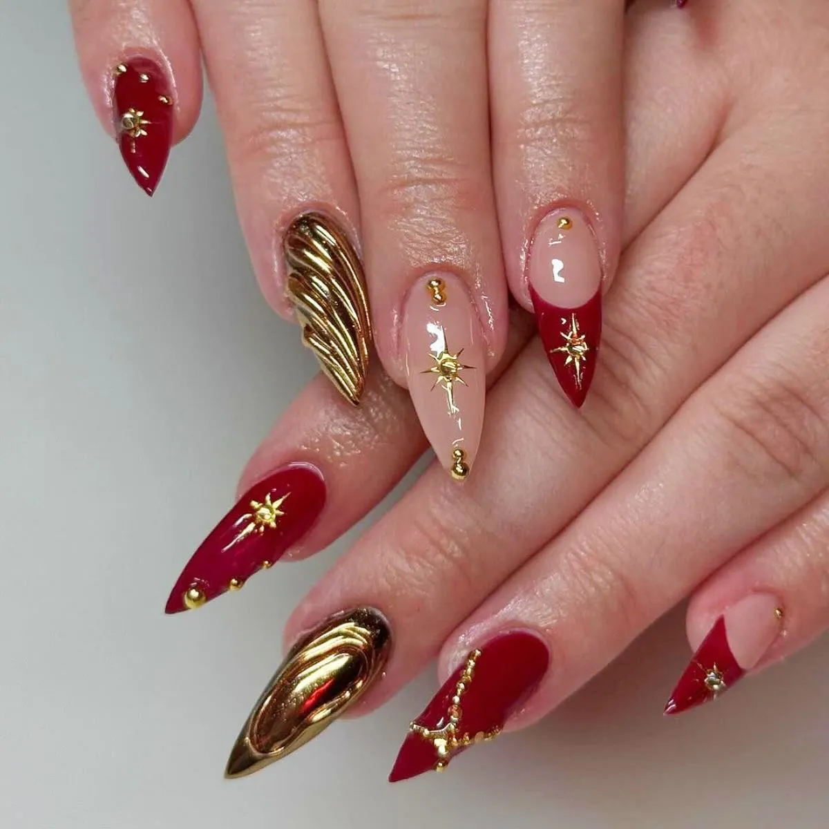 Pointed red-and-nude set with gold starbursts and ridged gold nails