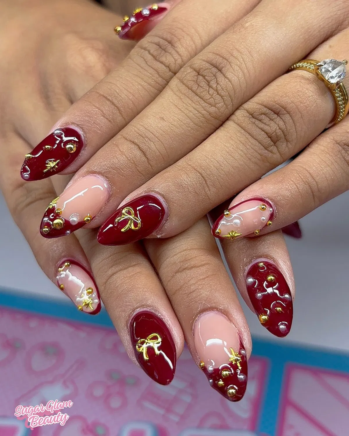 Deep red and nude nails with gold studs, stars, and bow motifs