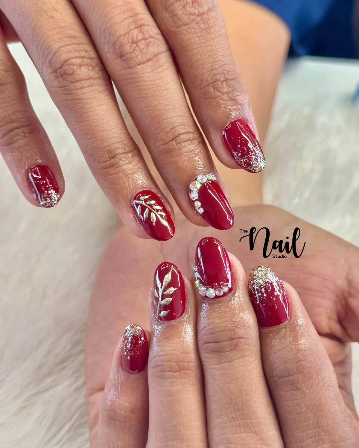 Deep red nails with gold leaf branches, glitter tips, and gem arcs