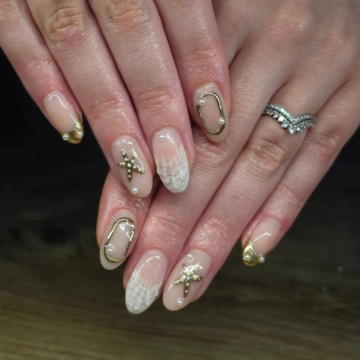 Nude oval nails with gold frames, starfish accents, and white grid pattern