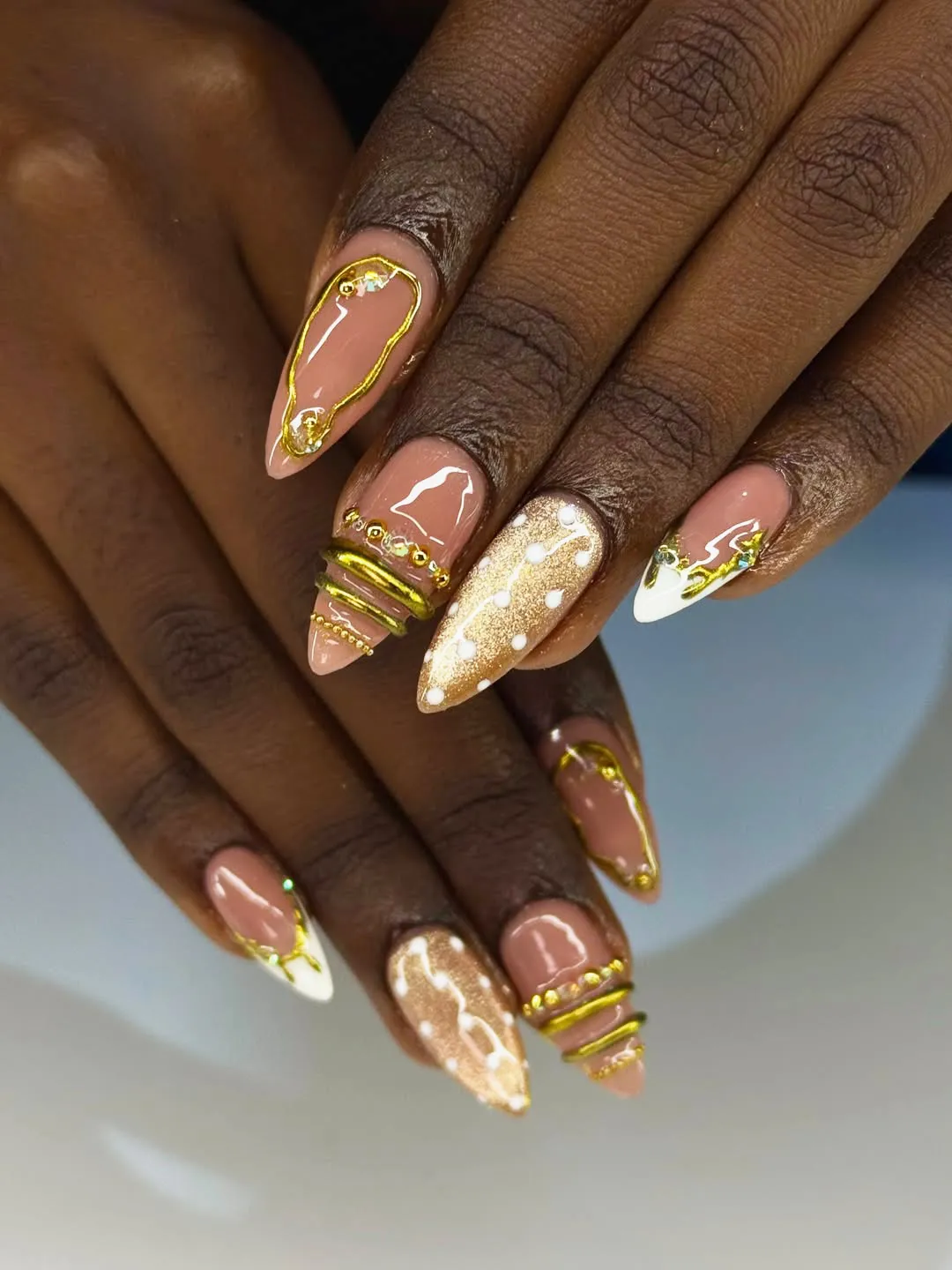 Nude almond nails with gold frames, metallic accents, and white dot details