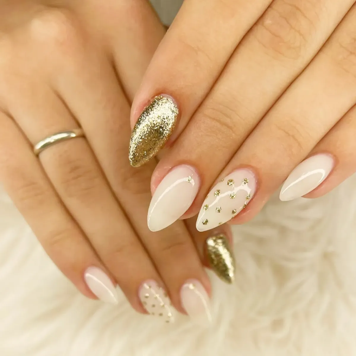 Milky white almond nails with gold glitter accents and gold studs
