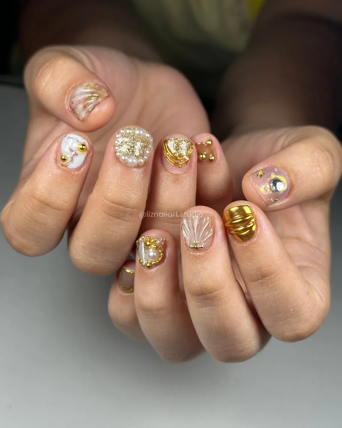 Short nude nails with pearls, studs, and gold 3D accents