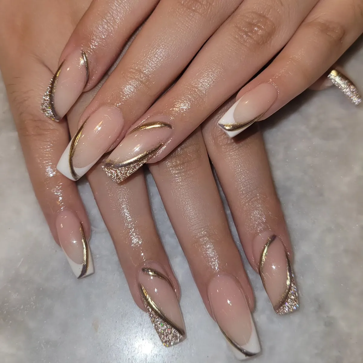 Square nude nails with white tips, gold glitter, and sweeping gold lines