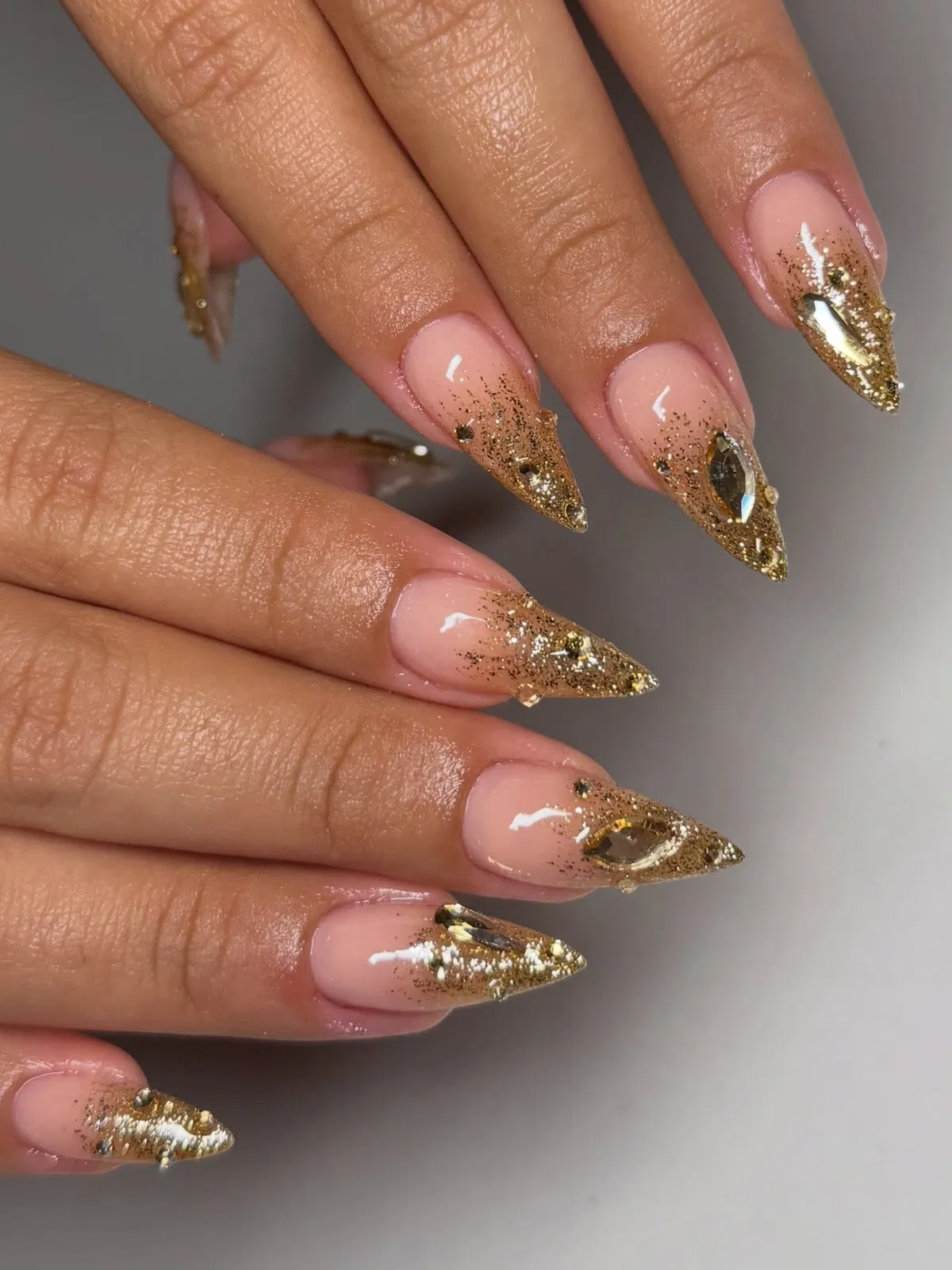 Nude stiletto nails with gold glitter tips and marquise rhinestones