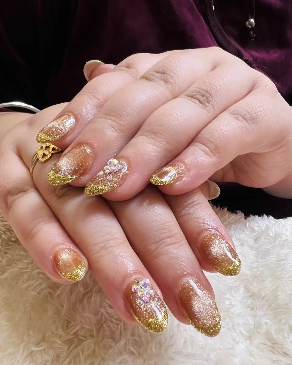 Gold shimmer nails with glitter tips and rhinestone clusters