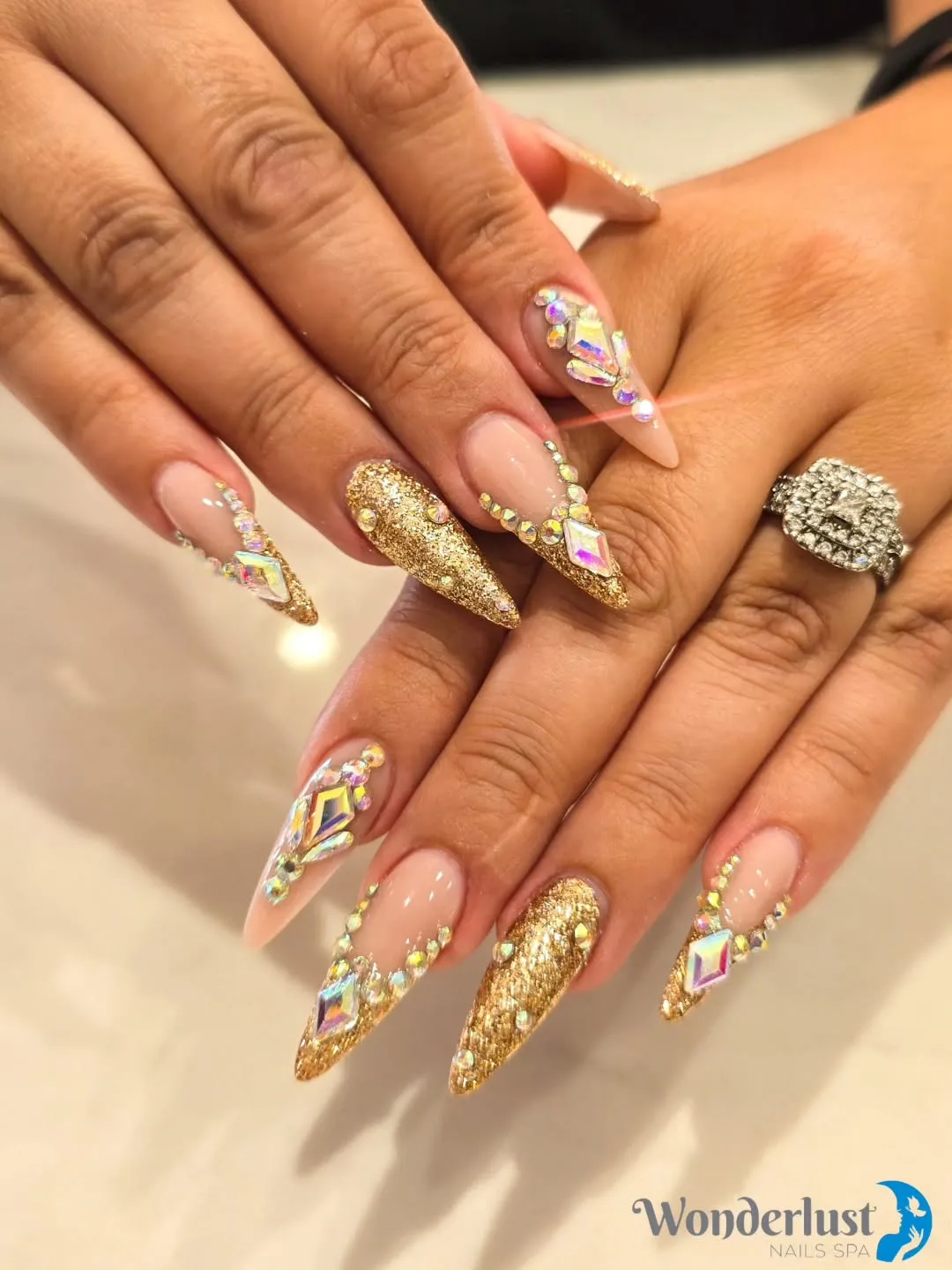 Long stiletto nude-and-gold glitter nails with iridescent rhinestones