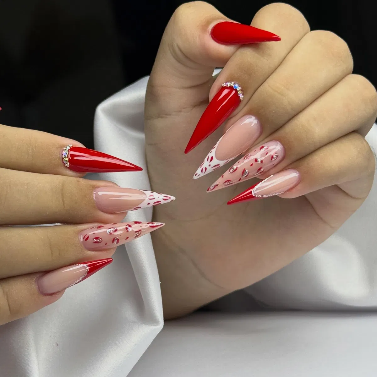 Red stiletto nails with rhinestone cuticle arcs and patterned accents