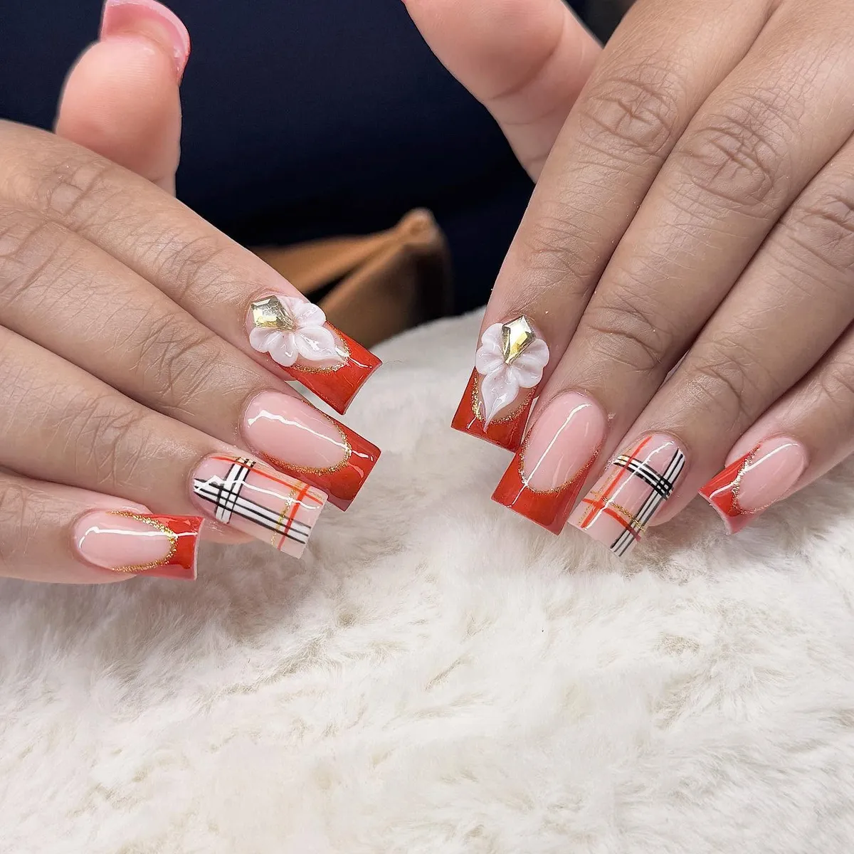 Orange French tips with plaid accents and floral gem details