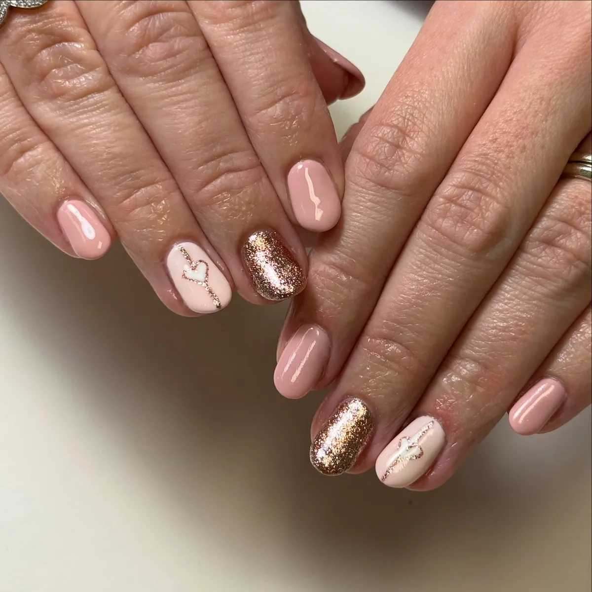 Pale pink nails with gold glitter accents and heart outlines