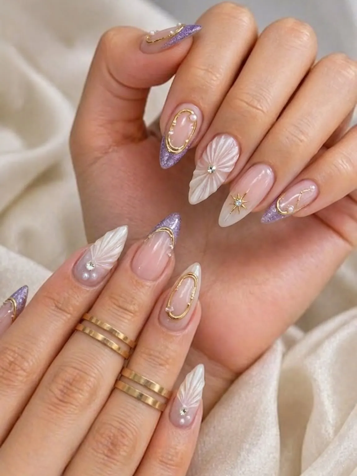 Nude almond nails with purple glitter tips, gold frames, and 3D white petals