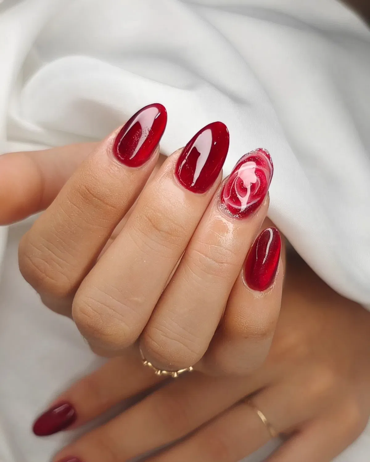 Glossy deep red nails with a red-and-white swirl accent