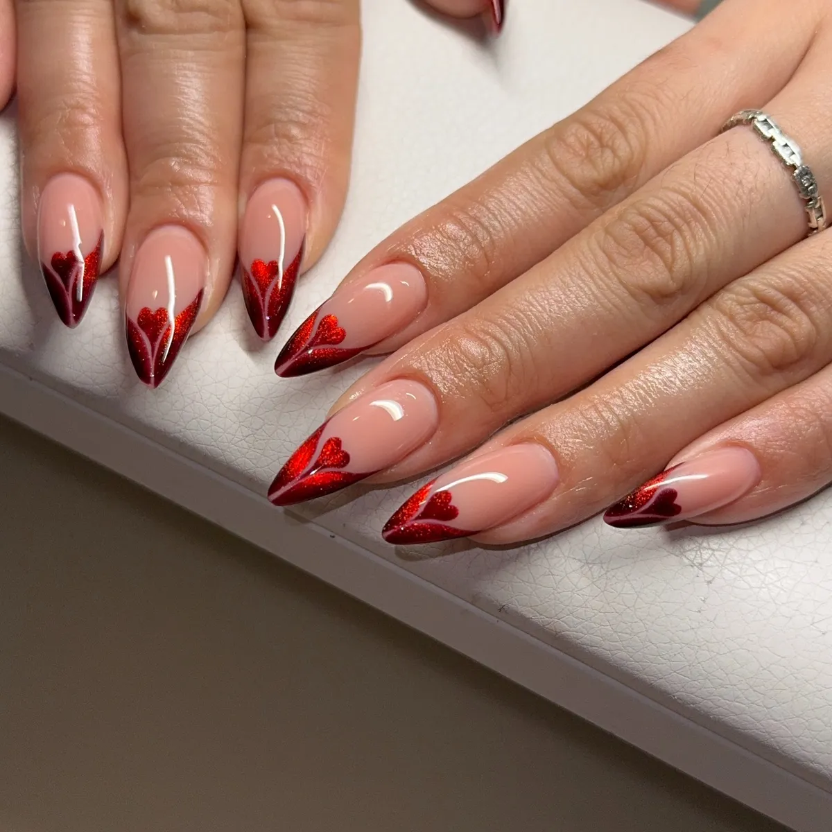 Nude stiletto nails with deep red V-tips and hearts