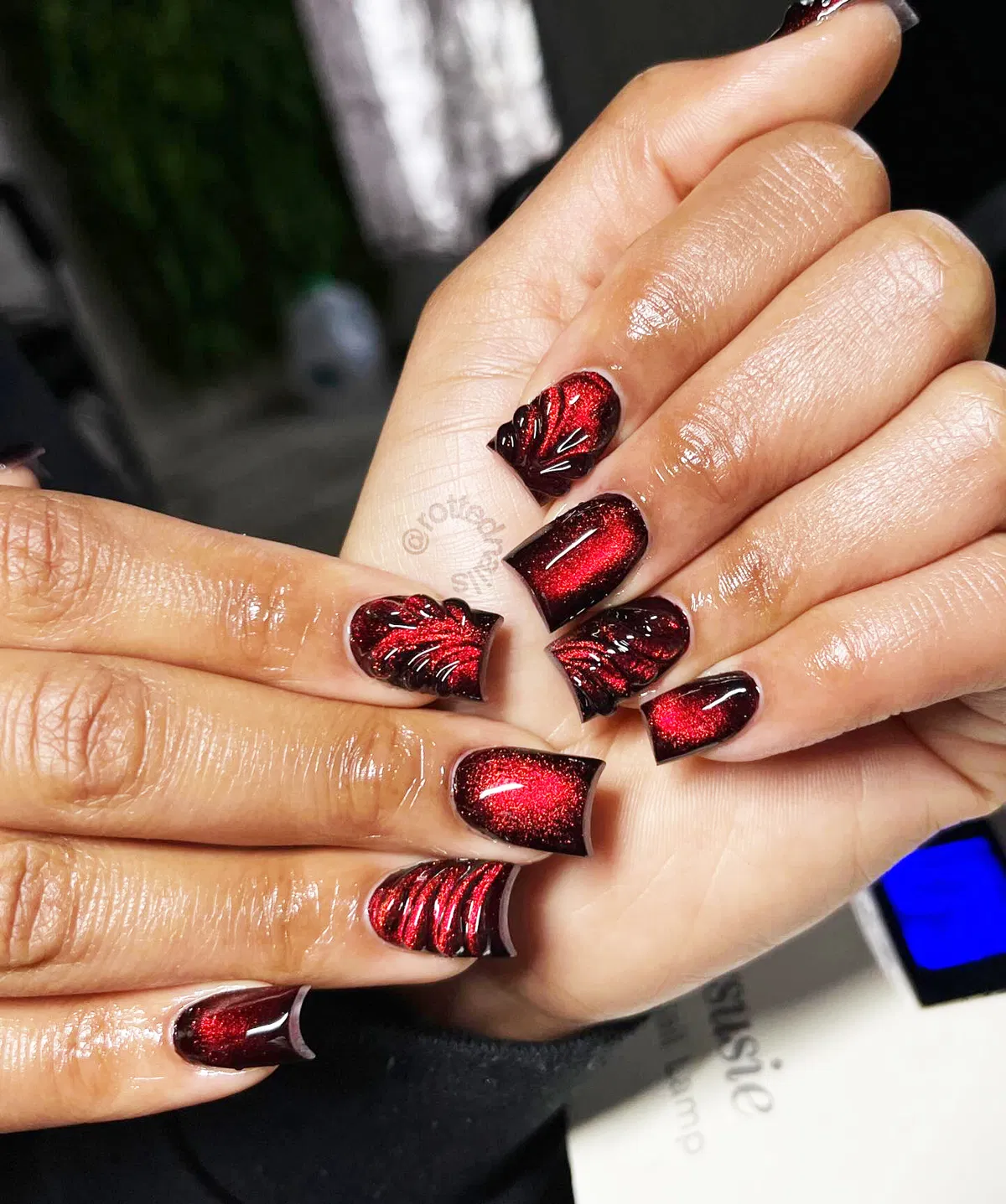 Red shimmer square nails with black framing and raised swirl accents