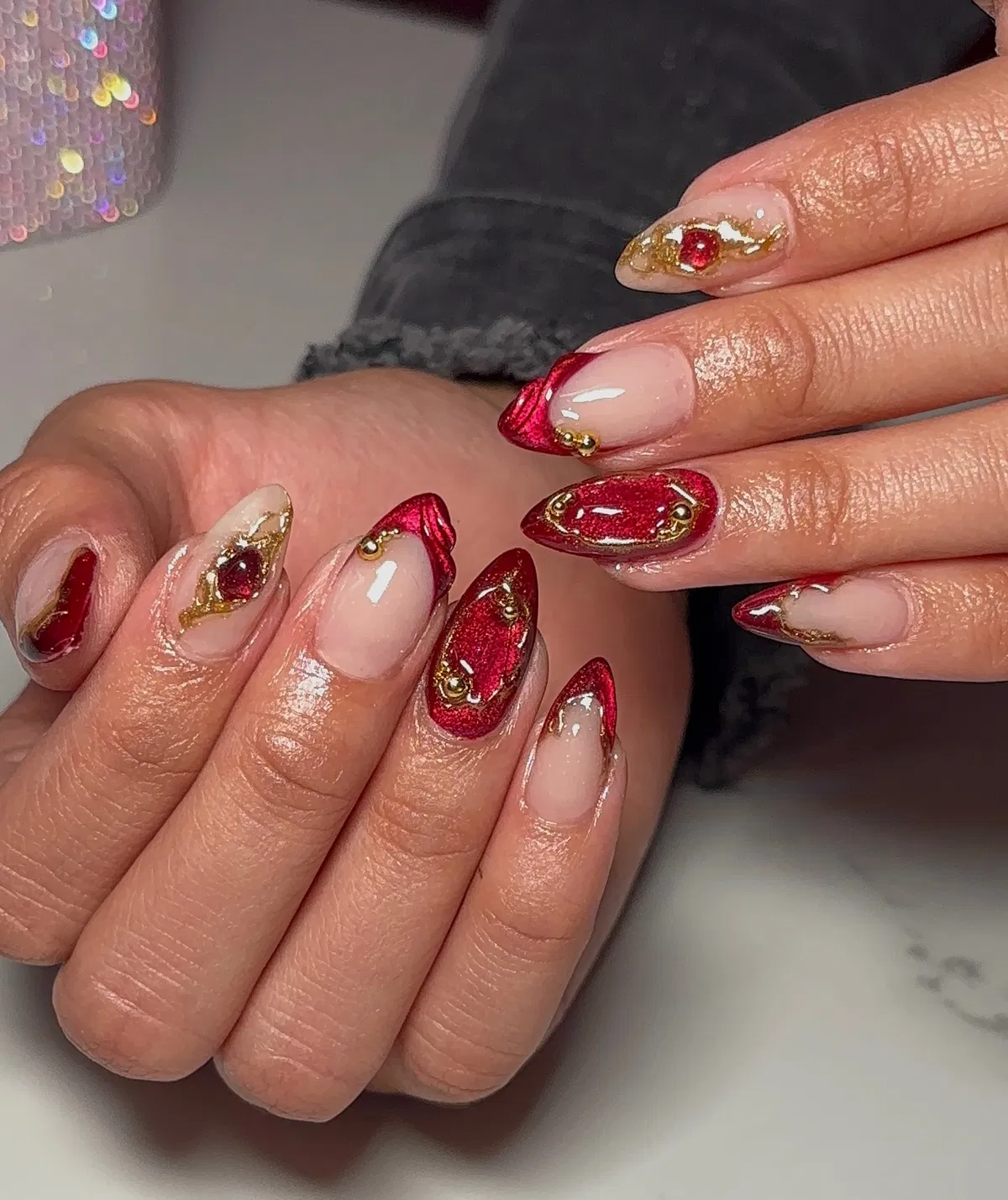 Red glitter almond nails with gold edging and studs