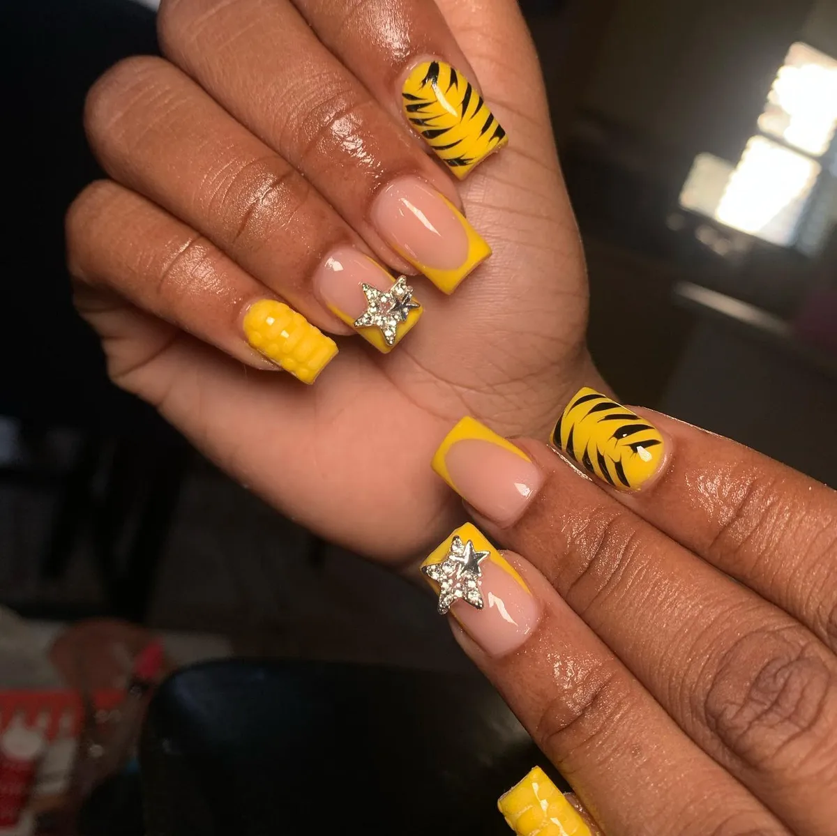 Yellow French tips with black leaf pattern, star rhinestones, and textured accent