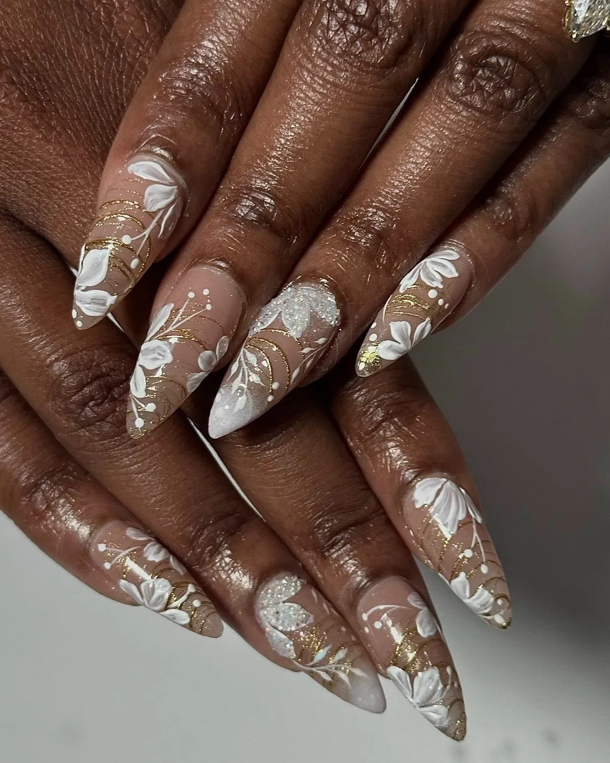 White floral and gold-line art on long pointed nails