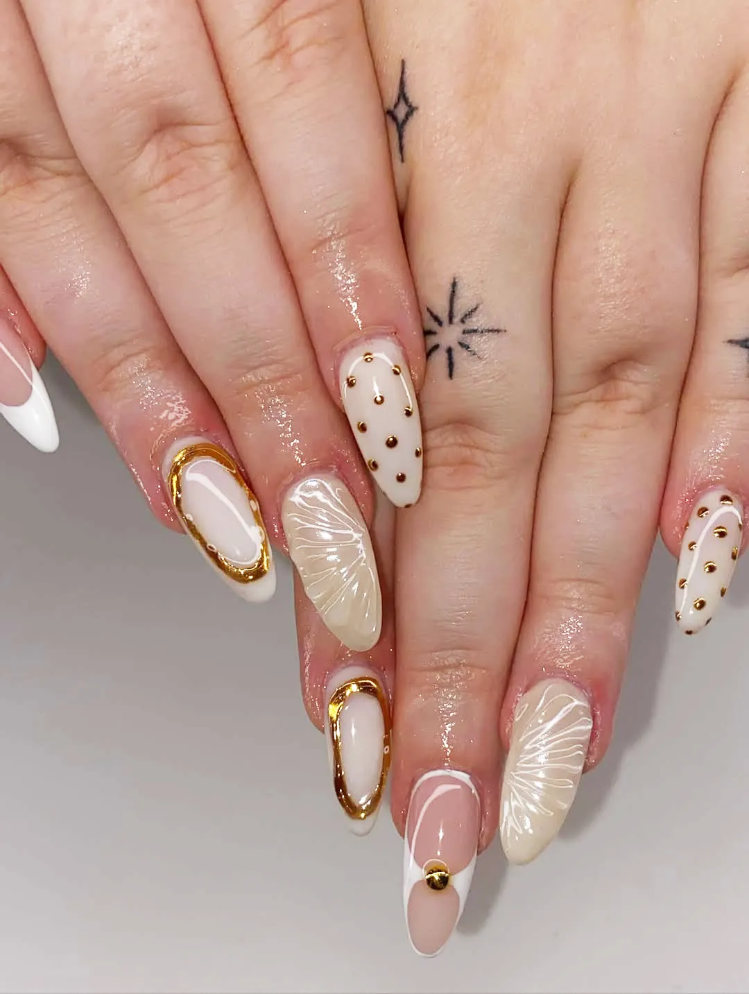 Gold-outlined almond nails with studs and white line-art florals