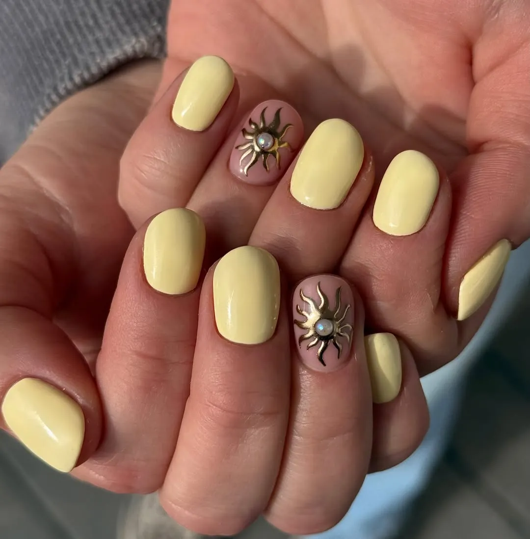 Pale yellow short nails with raised gold sun accents
