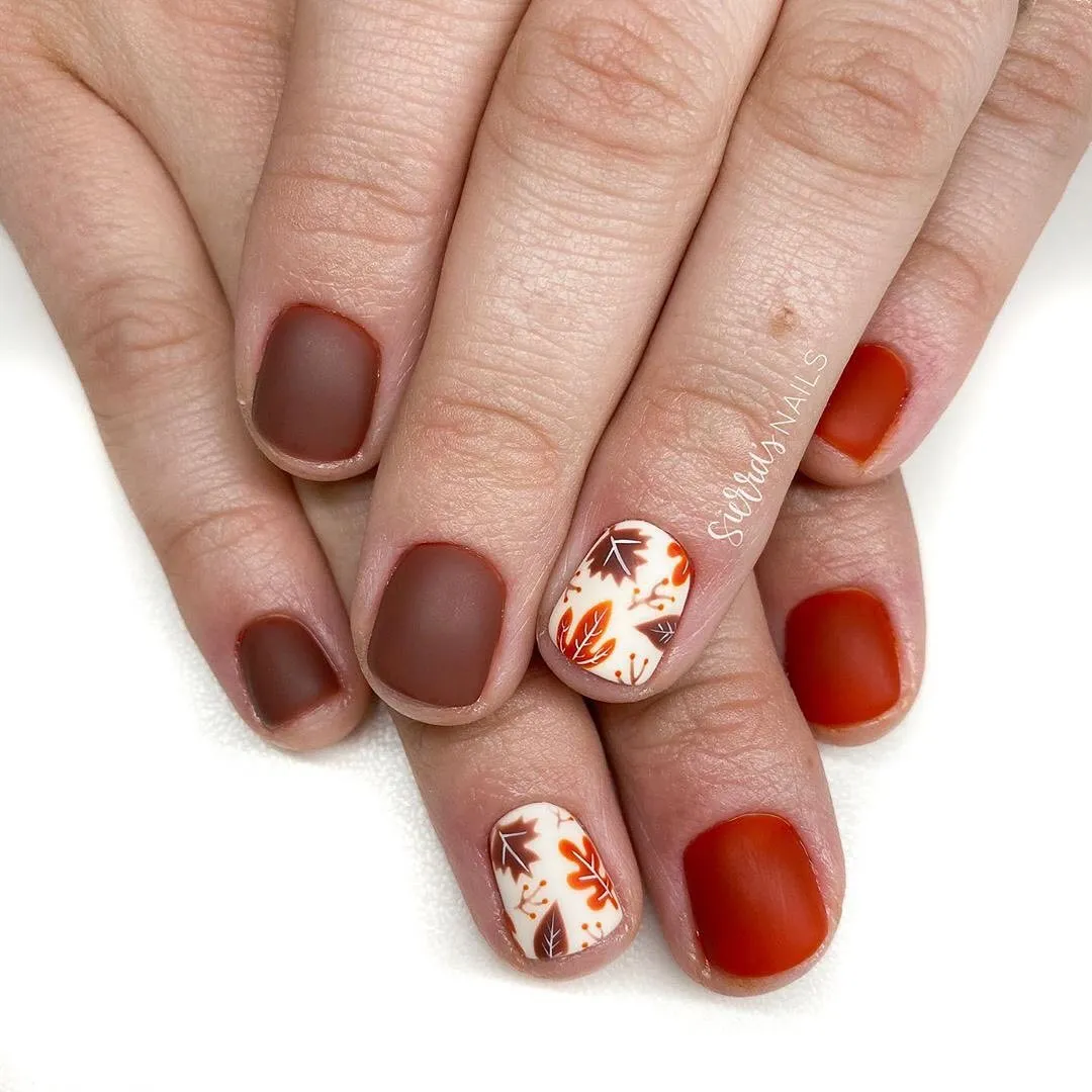 Matte brown and red-orange nails with cream leaf accents