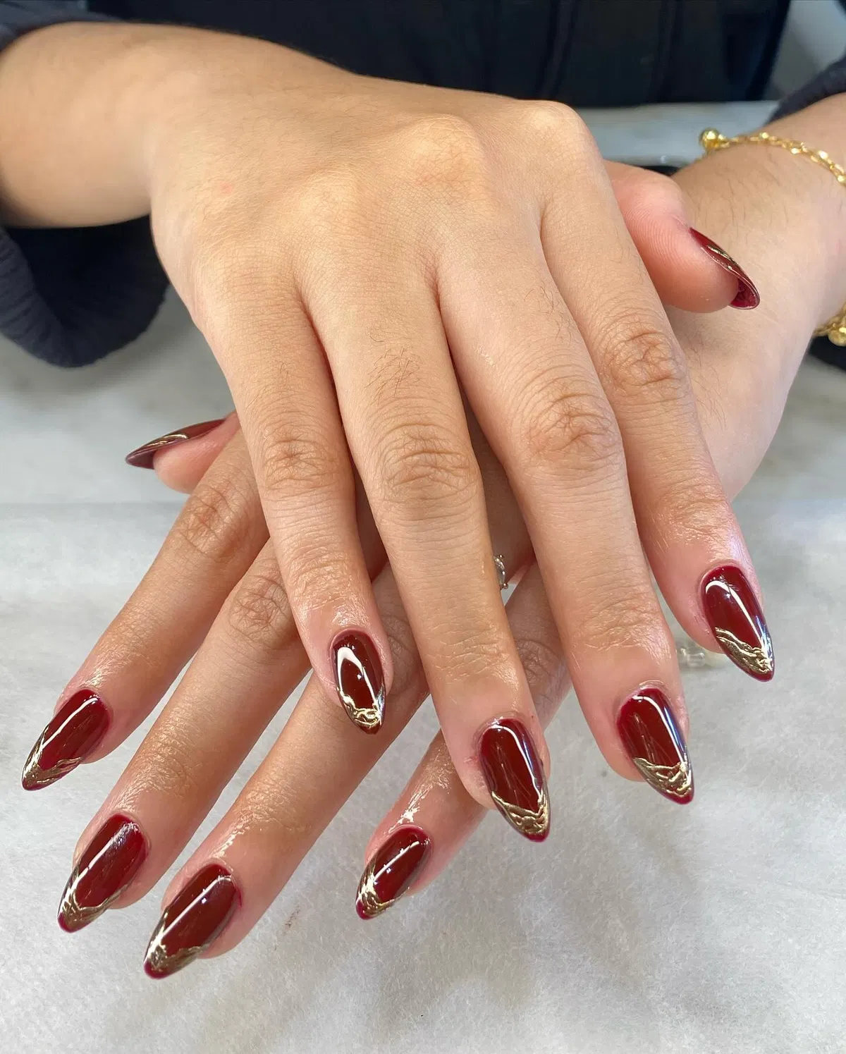 Deep red almond nails with gold metallic tip accents