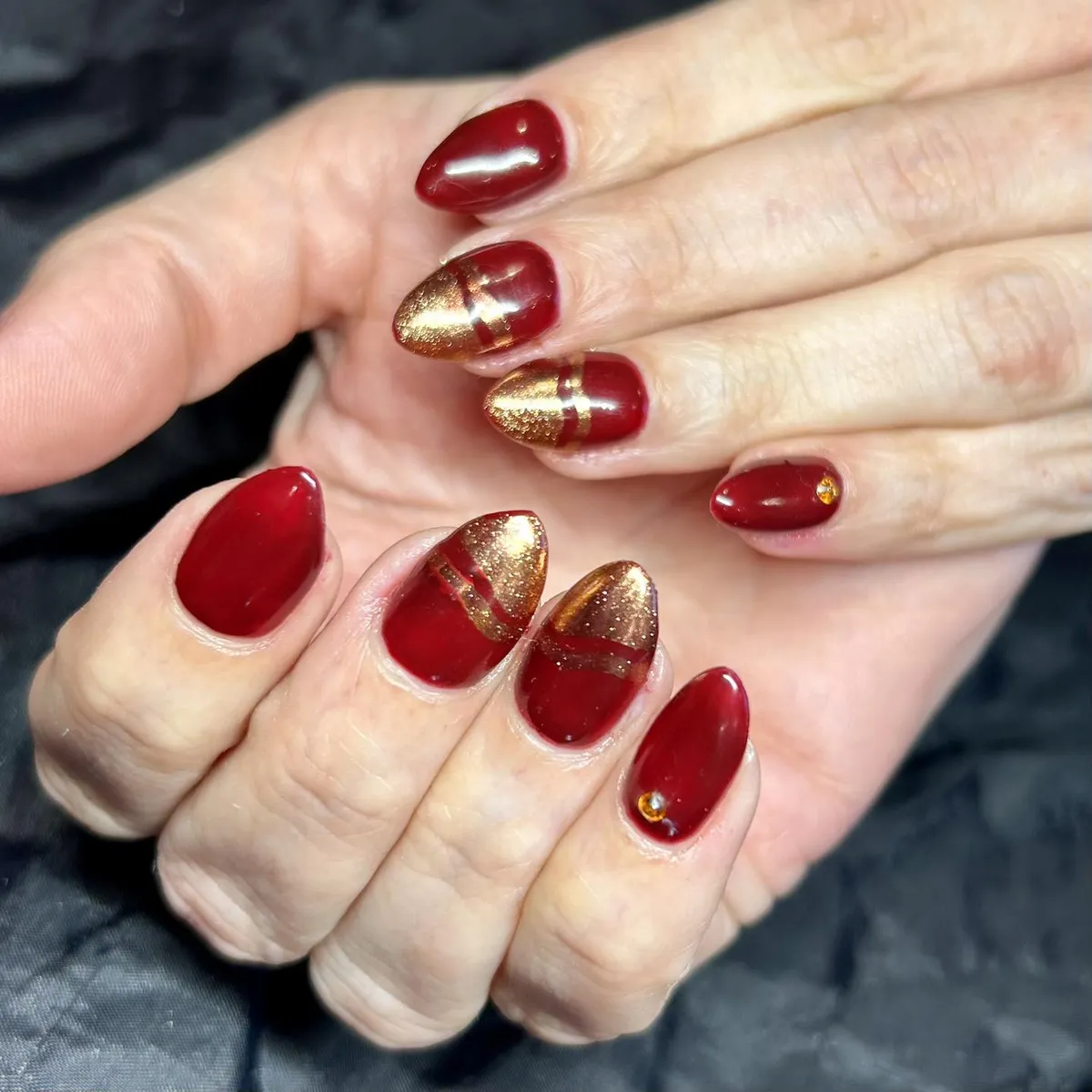 Deep red nails with gold glitter tips and small studs