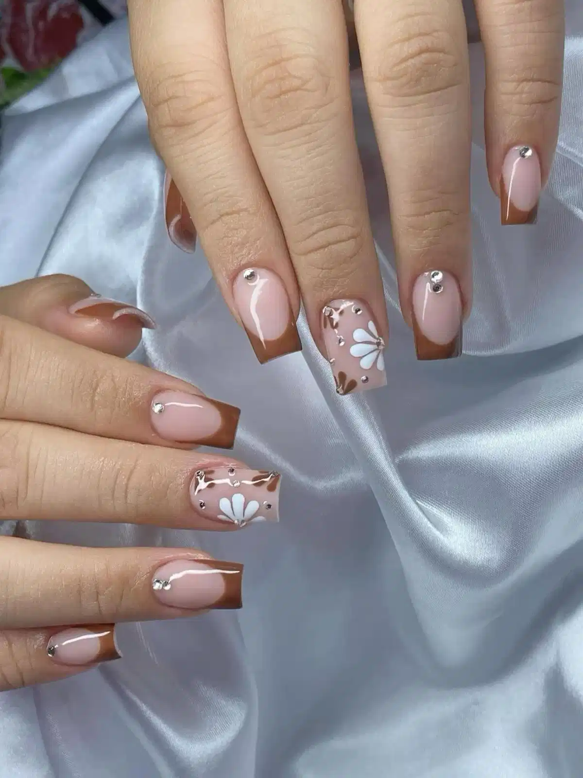 Brown French tips with white floral accents and silver studs