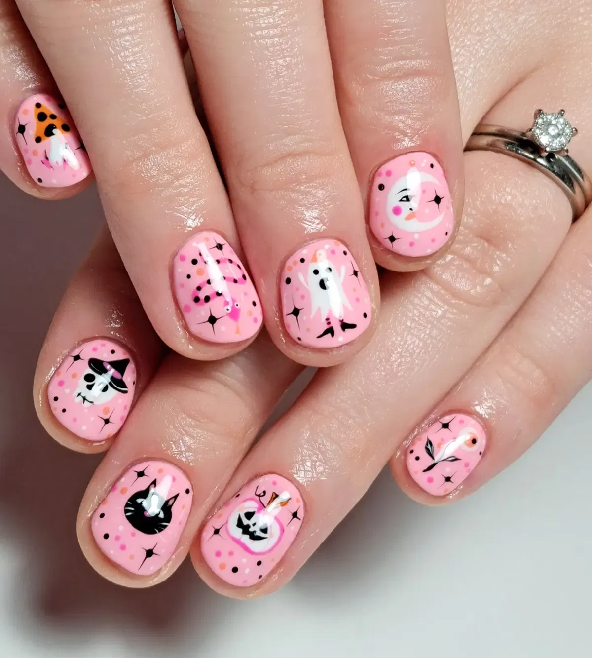 Pink nails with mini icons: ghost, cat, moon, web, and jack-o'-lantern