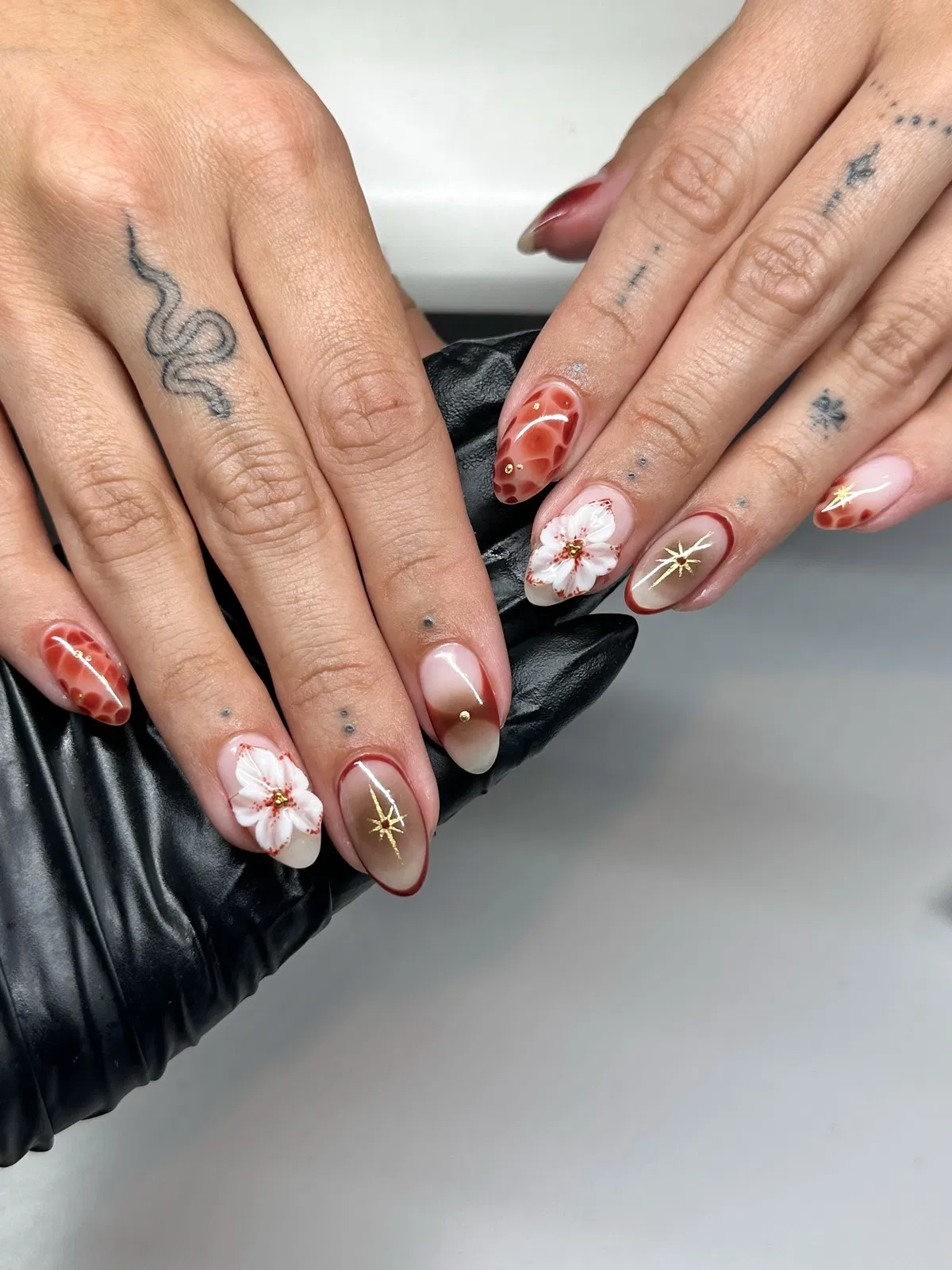 Nude base with reddish-brown outlines, white floral accents, and gold starbursts
