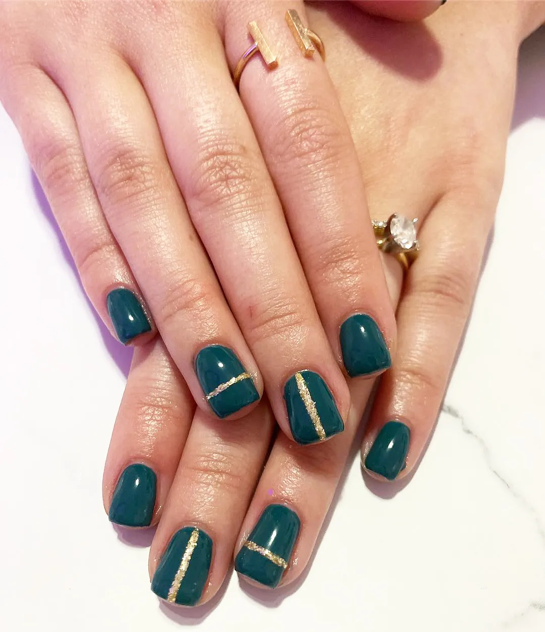 Teal-green nails with thin gold stripe accents