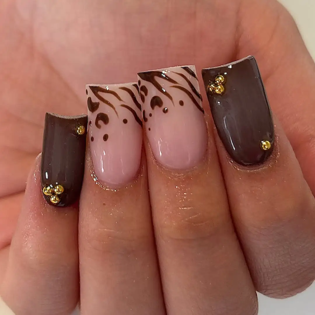Square dark brown and nude-pink nails with brown swirl detailing and gold studs