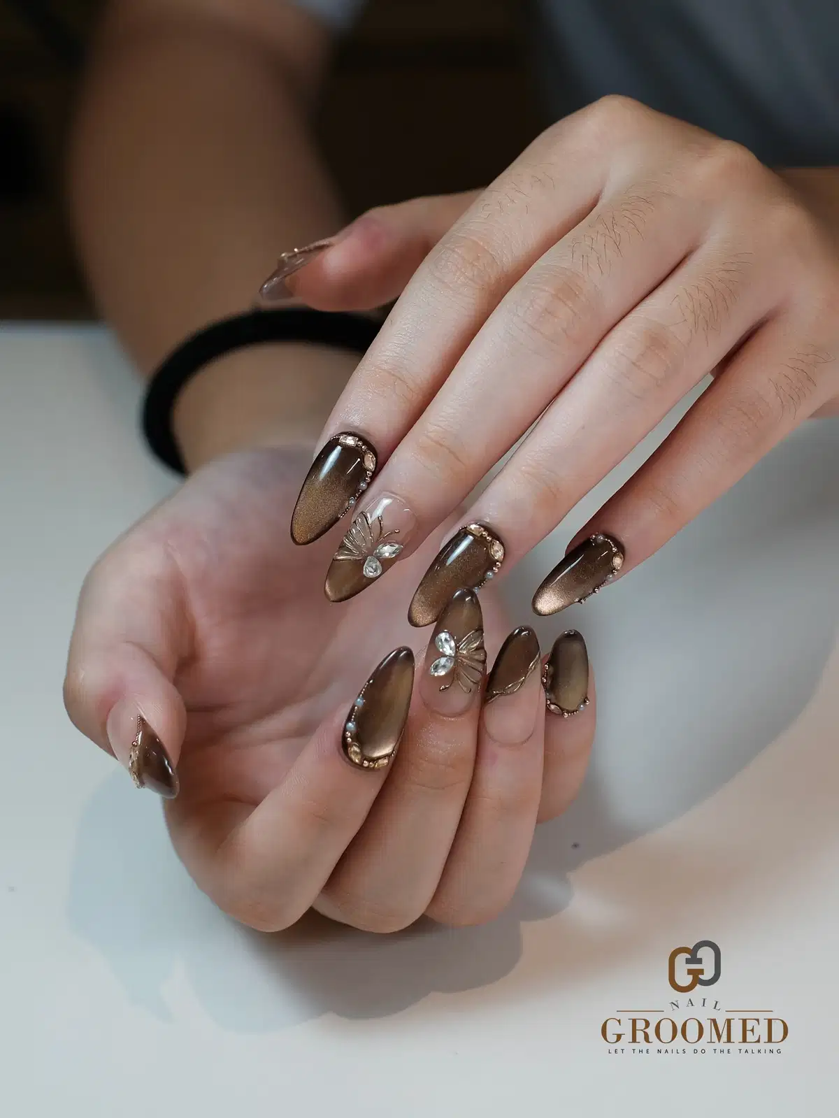 Long brown metallic-gradient nails with rhinestone borders and floral accents