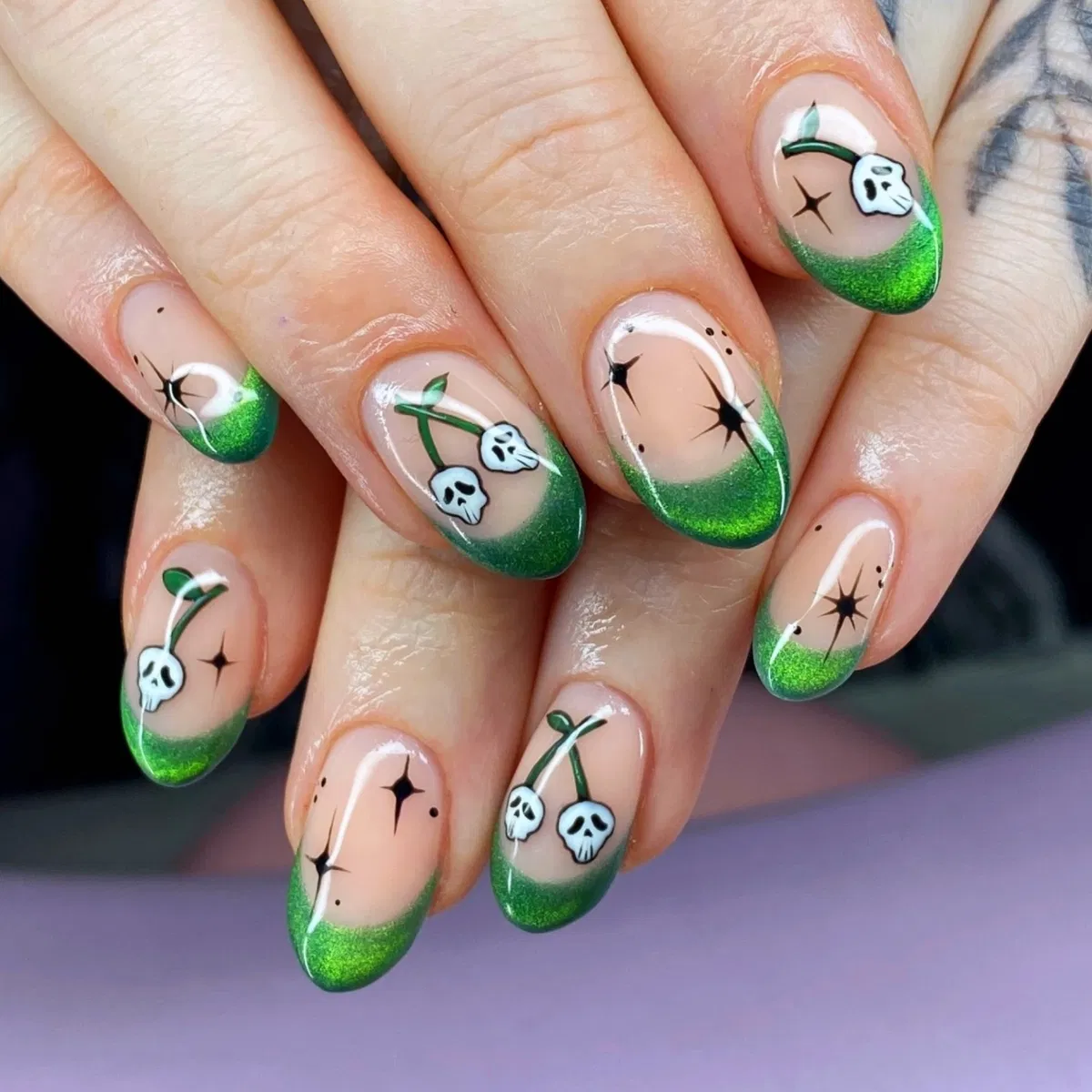 Nude nails with green glitter tips and skull-on-stem motifs