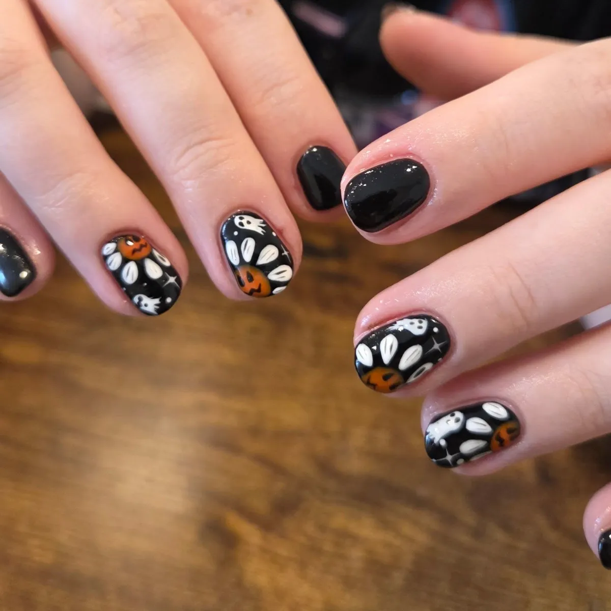 Black nails with white florals, ghosts, and orange pumpkins