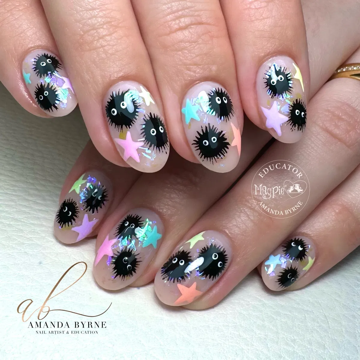 Sheer nude nails with black fuzzy-eyed motifs and pastel star confetti