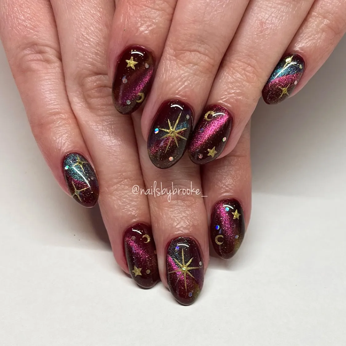 Dark glossy nails with magenta sheen and gold stars/crescents