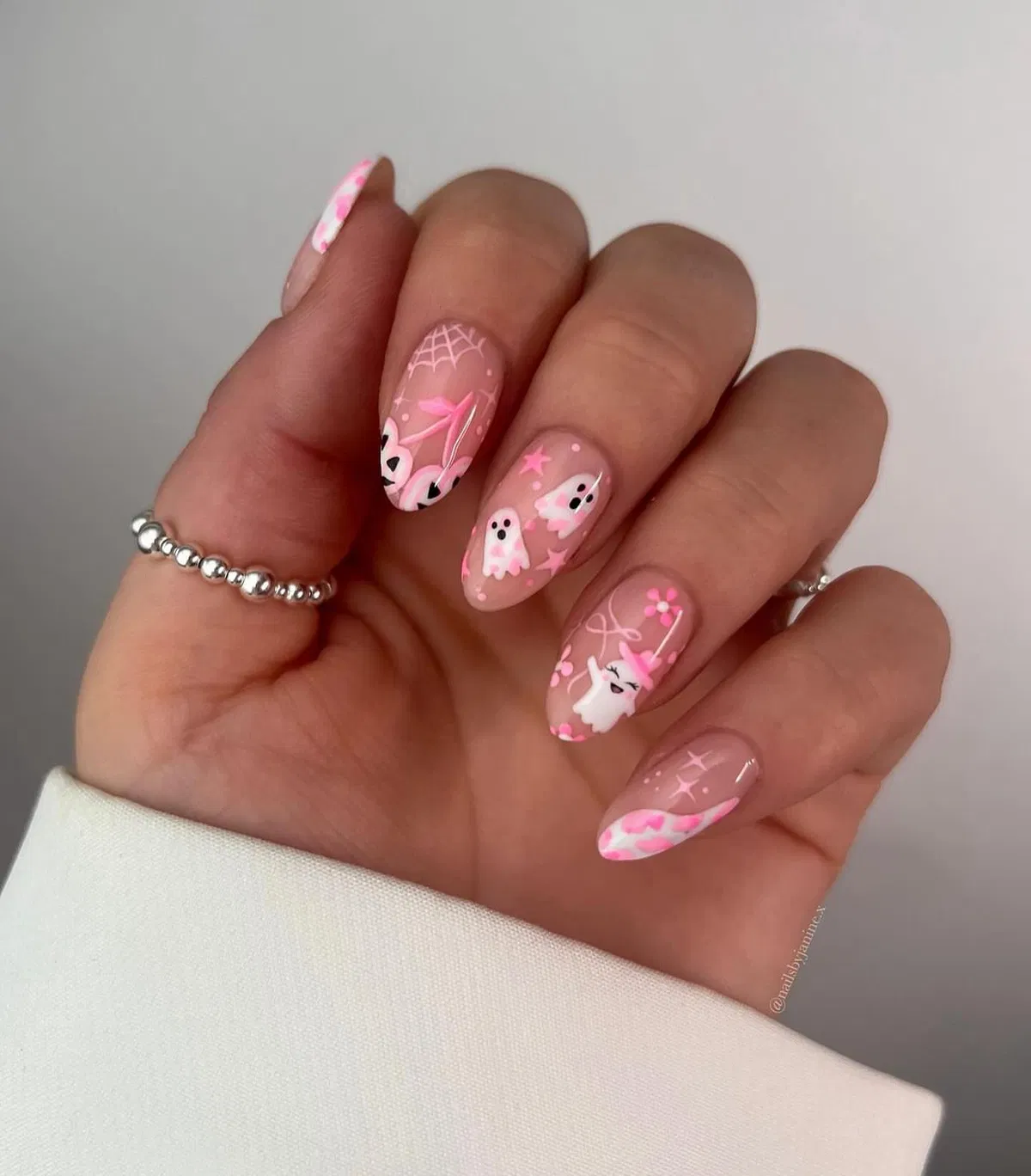 Sheer nude-pink almond nails with tiny ghosts and web detail