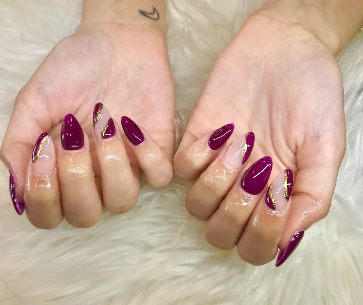 Deep plum almond nails with gold foil-style diagonal accents
