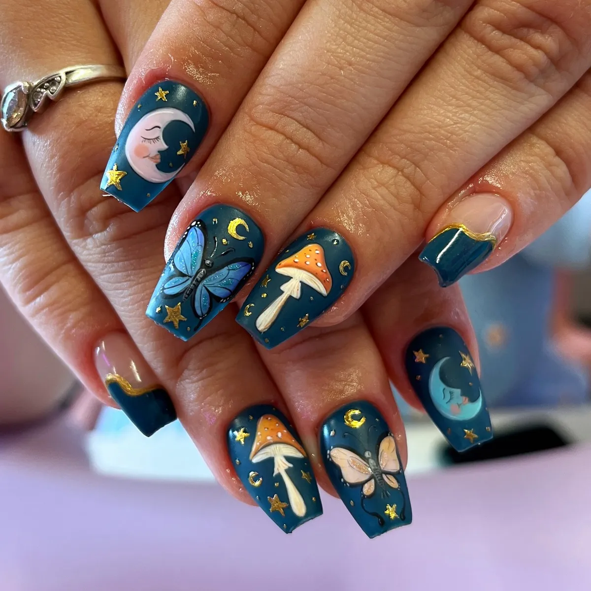 Teal square nails with gold stars, butterflies, and mushrooms