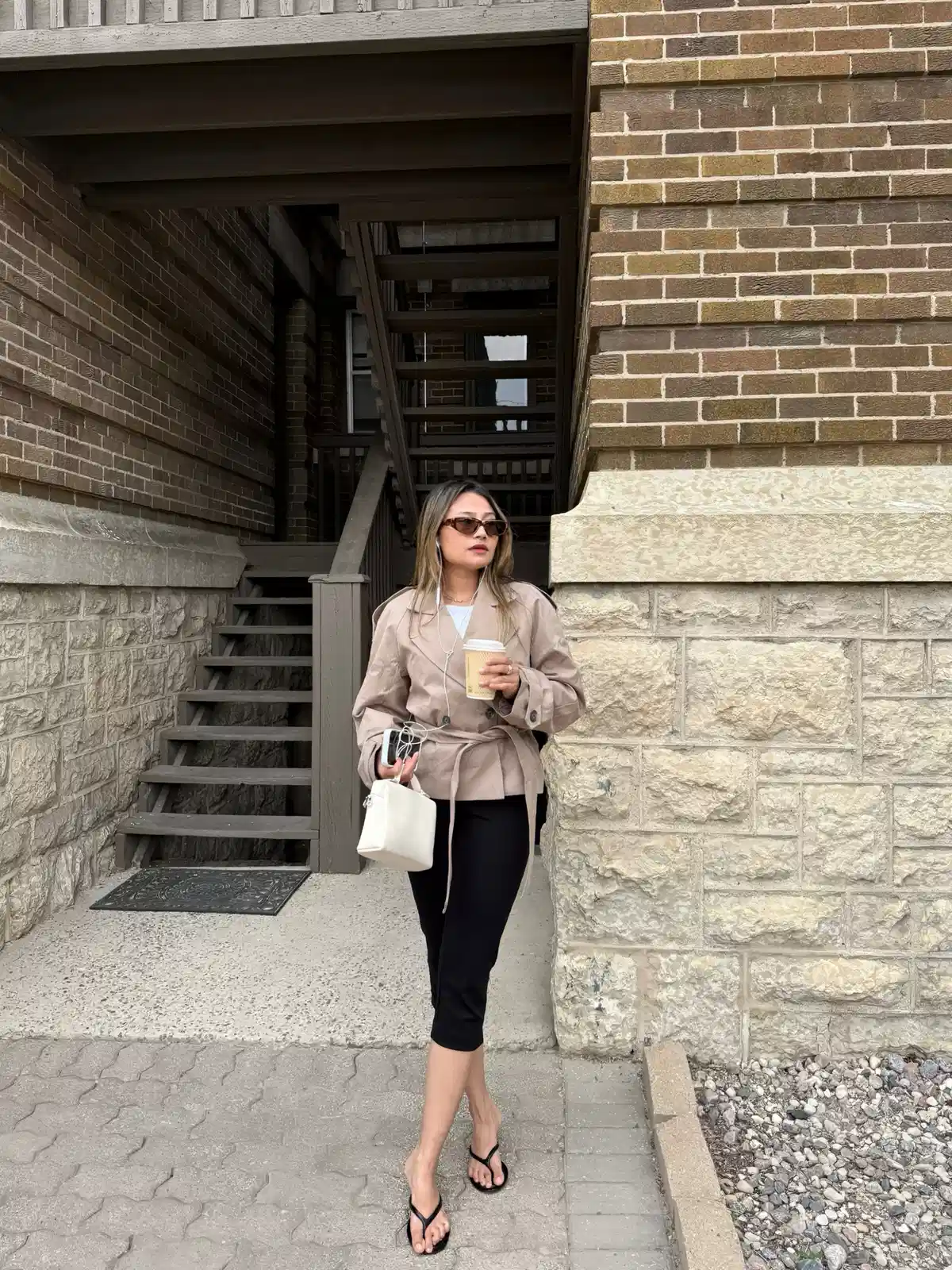Beige belted jacket with black leggings and flip-flops