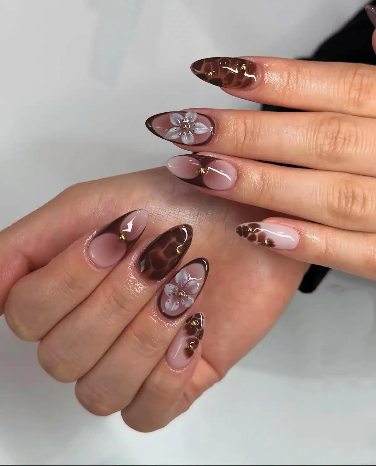 Sheer nude and chocolate tips with white floral accents and gold studs