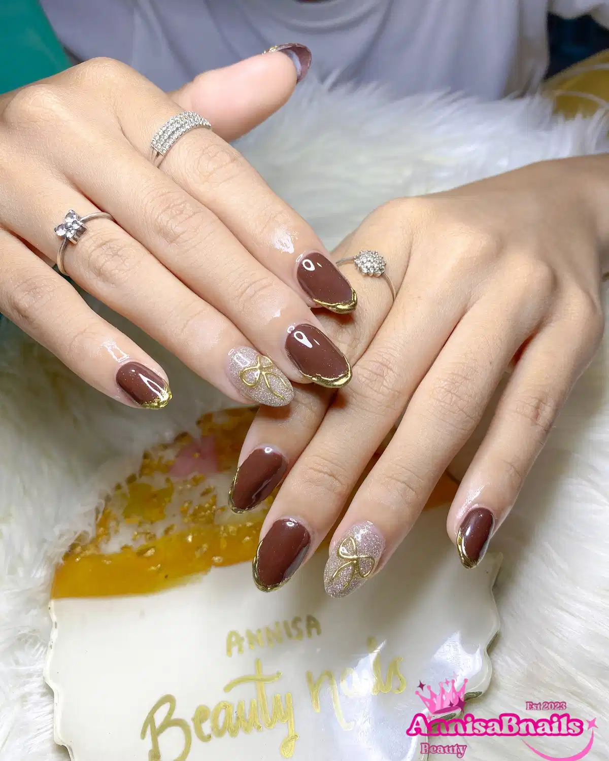 Brown nails with gold-edged tips and glitter bow accents