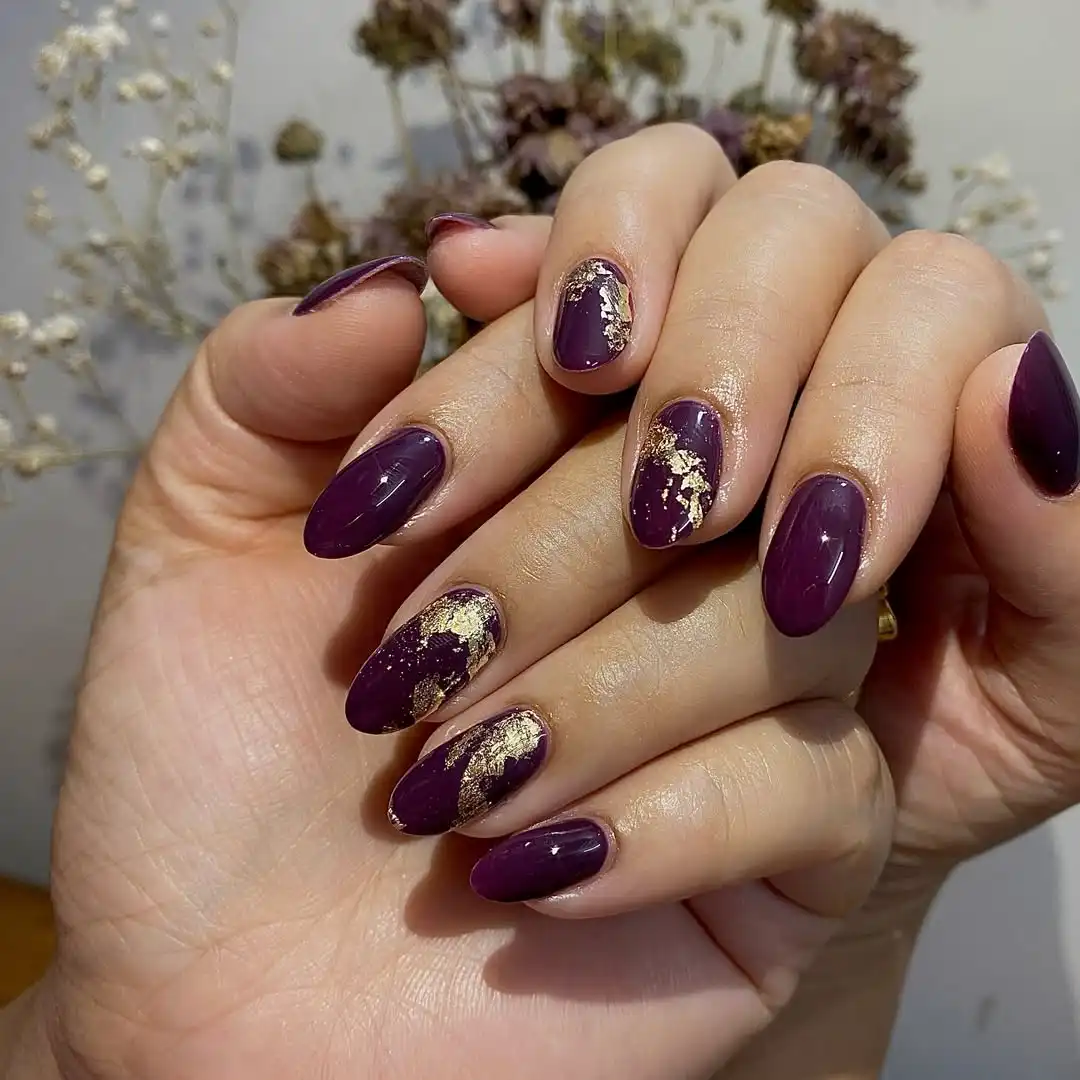 Deep plum nails with scattered gold foil accents