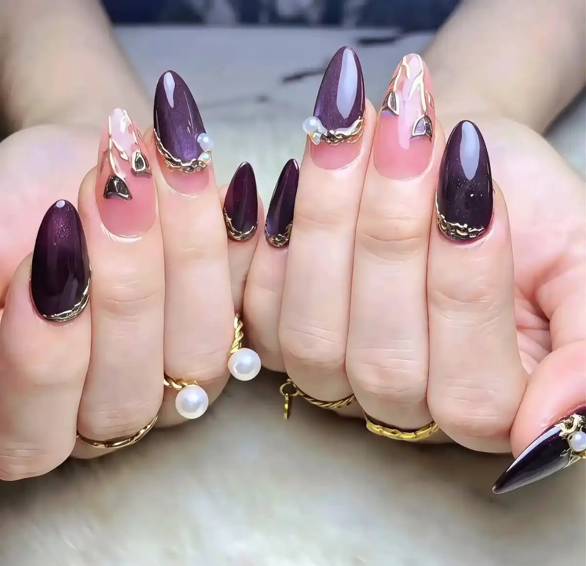 Dark purple and pink gradient nails with gold trim and stud accents