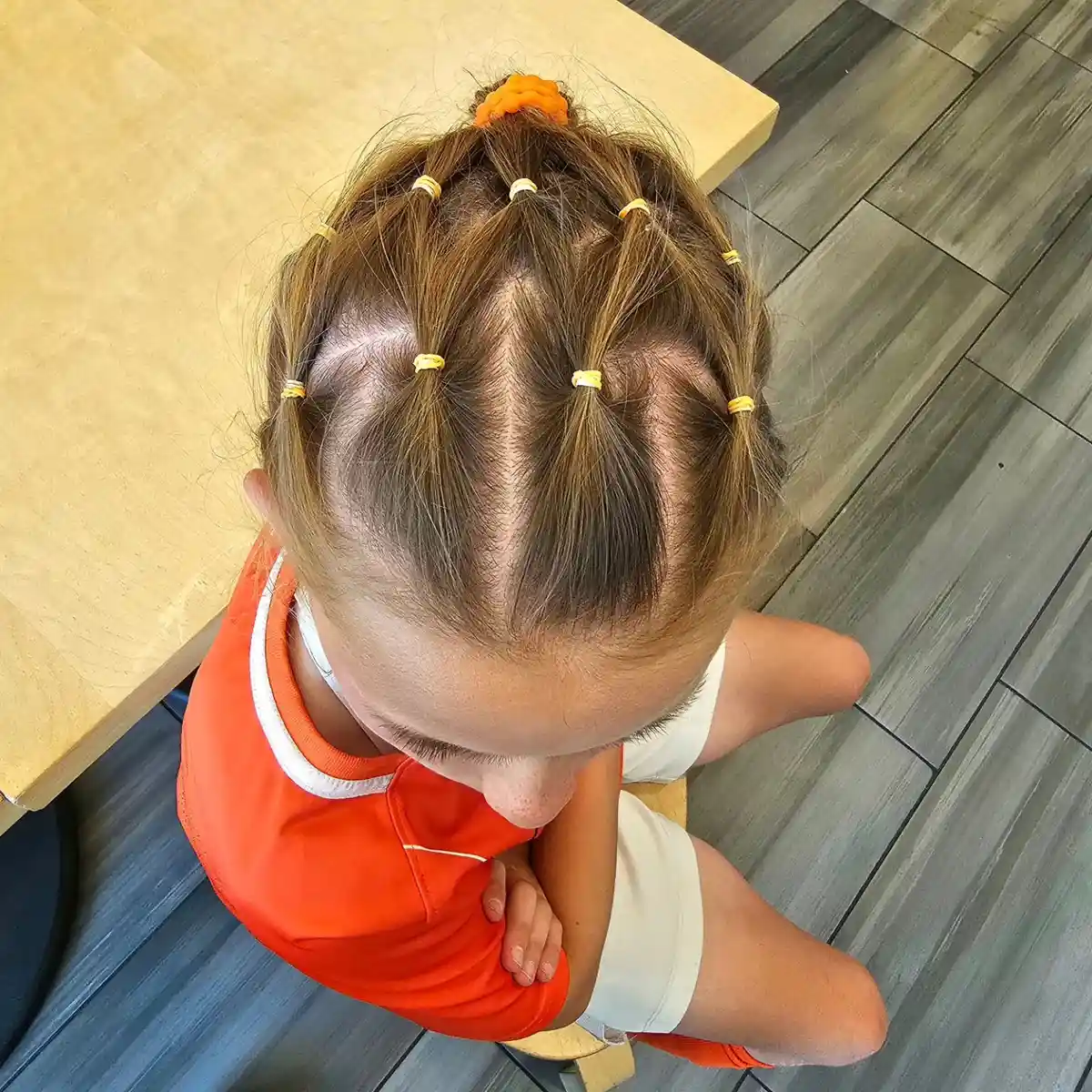 Grid-section ponytails with yellow elastics and orange scrunchie