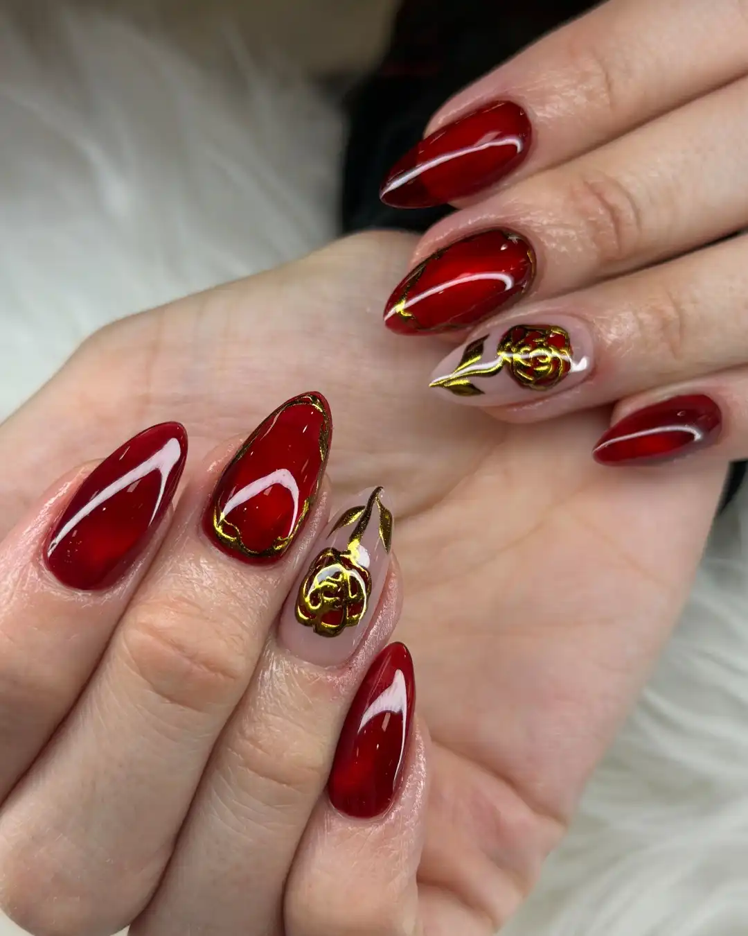Deep red almond nails with gold edging and raised rose accents